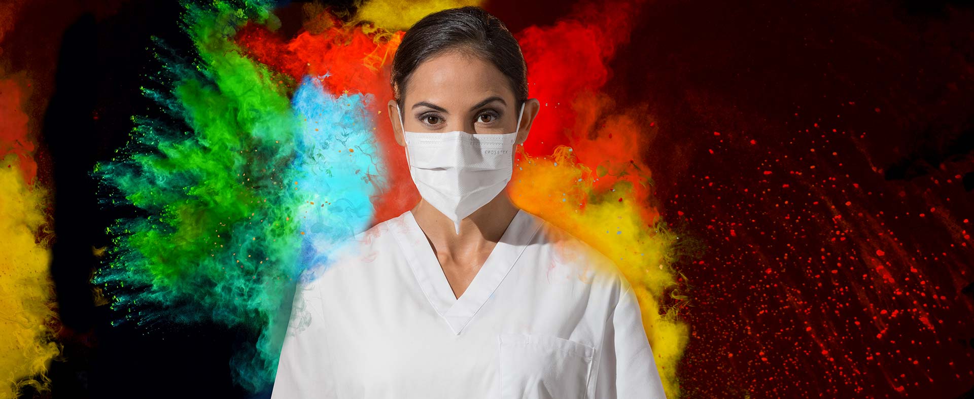 Woman in lab coat wearing Crosstex Mask with colored powder exploding around her