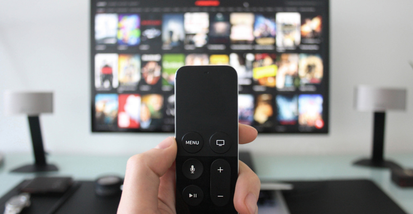 Person Holding Streaming Video Remote in Front of Blurred Connected TV