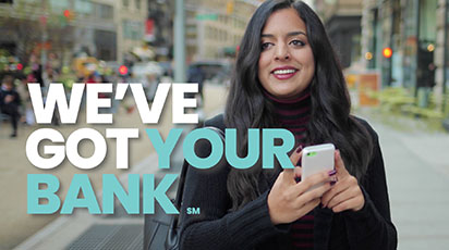A smiling woman with long dark hair stands on a city street, looking at her smartphone. Text overlay reads, 