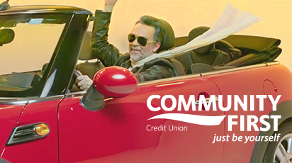 A man wearing sunglasses and a scarf waves from a red convertible car with the top down. The text 