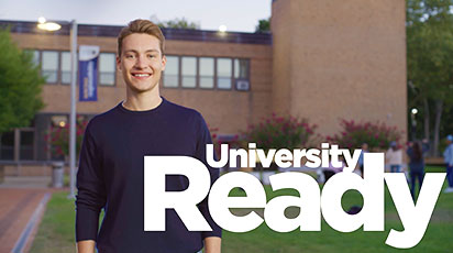 A young person stands outdoors on a college campus, smiling at the camera. Behind them is a brick building with large windows and greenery. The words 