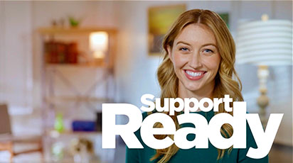 A woman with long, light brown hair smiles warmly at the camera. She is indoors with a blurred background showcasing a well-lit room with shelves and a lamp. The text 