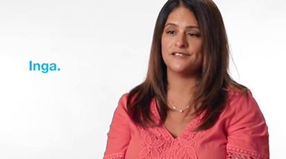 A woman with long brown hair wearing a coral blouse is speaking. The background is plain white, and the name 