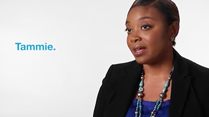 A person wearing a black blazer and a beaded necklace is speaking against a white background. The name 