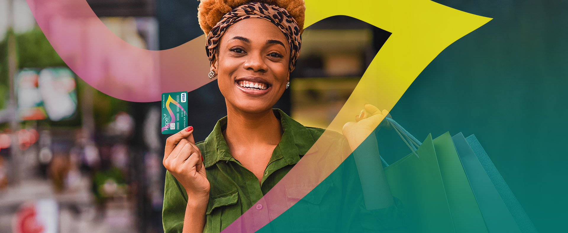 A smiling woman in a green shirt holds a credit card in one hand and shopping bags in the other, with colorful swoosh patterns in the foreground. The background shows a blurred city street scene.
