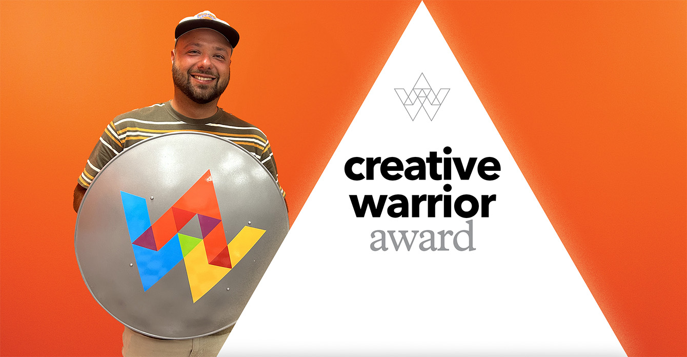Stephen standing in front of orange wall holding a shield with the Austin Williams logo on it.